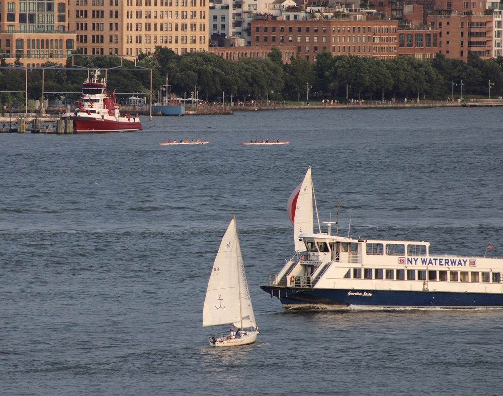 A NY Waterway ferry passes two small sailboats on the Hudson in front of the Manhattan waterfront