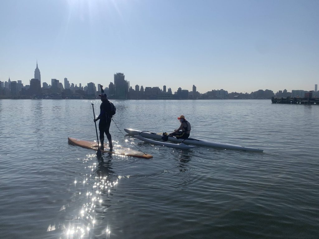 A stand-up paddler and a two-person outrigger canoe on the Hudson on a calm morning